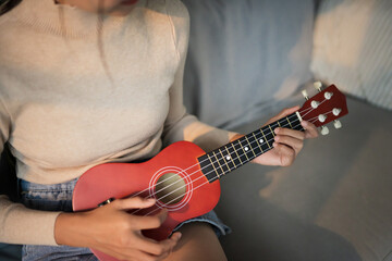 Happy young female asian woman playing ukulele and singing relaxing on couch at home Girl learning to play the ukulele 
