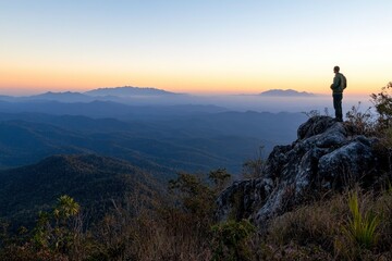 A man standing on top of the mountain, overlooking distant mountains and clear sky at sunrise with copy space for text. A hiker stands in awe as they look out over the vast landscape from atop Pui