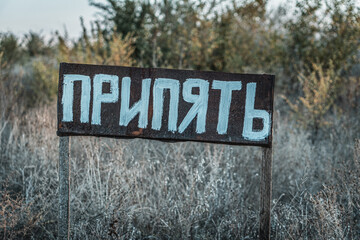 Fototapeta premium A weathered sign with the word 'Припять' in Cyrillic script, standing in an overgrown, abandoned area.