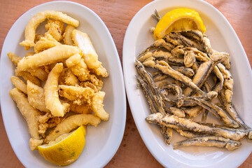 Two plates of freshly fried fish with lemon wedges. The left plate contains golden-brown fried fish...