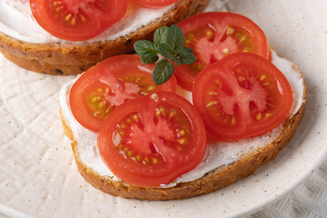 Delicious open-faced sandwiches topped with fresh tomatoes and cream cheese served on a textured white plate