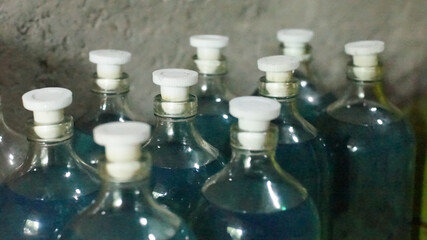 A collection of glass bottles containing blue gasoline with white bottle caps