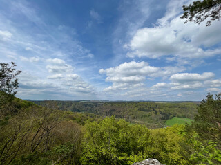 Panoramic view of mountains and trees under blue sky with clouds in the Mullerthal region, Luxembourg.