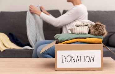 Female Volunteer preparing used clothes for donation in a cardboard box at home