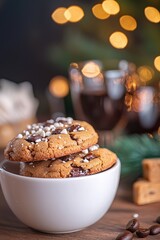 Fototapeta premium Delicious freshly baked chocolate chip cookies with sprinkles in a white bowl against a warm, festive background of blurred lights and coffee glasses