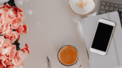 Spring home office background with copy space. Smartphone with pink flowers, laptop and coffee frame with copy space for design or product presentation