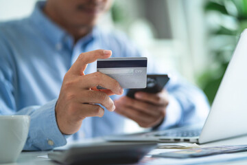 A man is holding a credit card and a cell phone, possibly using them to make a purchase