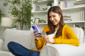 Attractive Asian woman using a smartphone to make purchases online, online shopping, enjoying leisure time on the weekend sitting on a sofa at home. asian female using credit card make online payment.