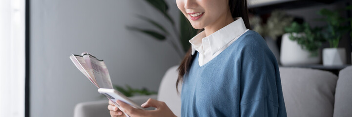 Asian woman holding paper document calculating money savings paying bills in mobile application...