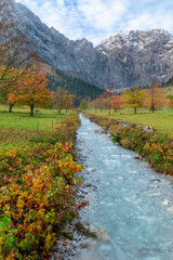 Colorful autumn landscape at Großer Ahornboden in the Karwendel Mountains, Austria – forest with fall foliage, rocky peaks and dramatic sky