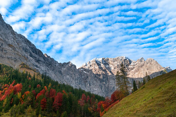 Colorful autumn landscape at Großer Ahornboden in the Karwendel Mountains, Austria – forest with fall foliage, rocky peaks and dramatic sky