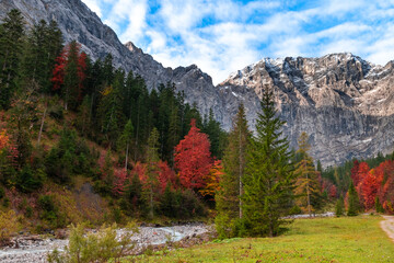 Colorful autumn landscape at Großer Ahornboden in the Karwendel Mountains, Austria – forest with fall foliage, rocky peaks and dramatic sky
