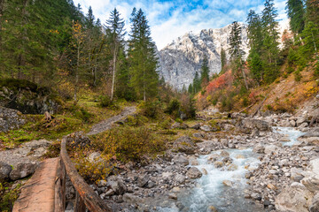 Mountain stream with wooden bridge and colorful autumn forest at Großer Ahornboden in the Karwendel Mountains, Austria – scenic alpine nature landscape