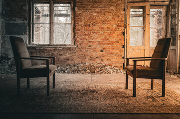 Two vintage chairs face each other in an abandoned room with brick walls, broken windows, and a...