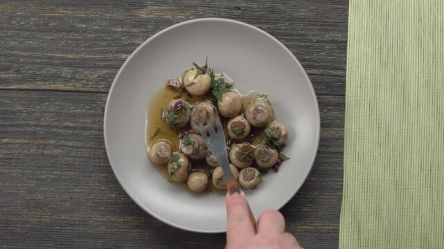 A fork spears and lifts marinated champignons with spices and marinade onto a plate. Top view. High quality 4k footage