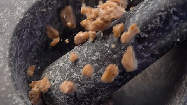 Large pieces of the sweet brown sugar are falling into the grey stone mortar in slow motion. High quality 4k footage