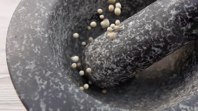 Spicy exotic white peppercorns are falling and bouncing in the grey stone mortar in slow motion. High quality 4k footage