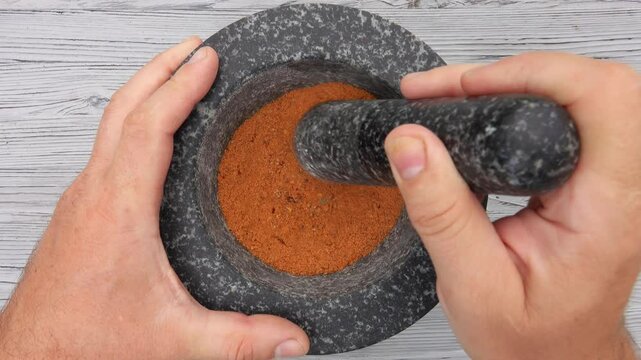 Top view of the hand with heavy pestle grinding mix of spices and peppers in the grey stone mortar. High quality 4k footage