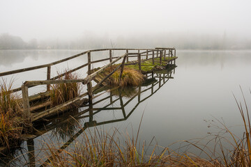 An old broken jetty on a foggy day on a mirror calm La Mouline, a lake in the village of Groléjac...