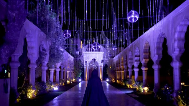Palais Namaskar - December 28, 2024: shows a person in a dark cloak walking through a beautifully lit, arched pathway adorned with hanging lights and reflective spheres in Marrakesh, Morocco, 4K