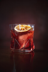A sophisticated cocktail served in a geometric glass, garnished with a dried orange slice, against a dark, moody background