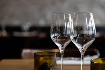 Two empty wine glasses on a wooden table in a softly lit restaurant setting, with a blurred background