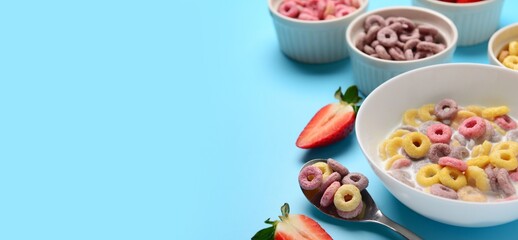 Bowls of different sweet cereal rings with milk and strawberry on light blue background with space for text, closeup