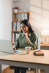 woman working on laptop at wooden table with cup of coffee, books, and notebook, in cozy home office with natural light and bookshelf in background