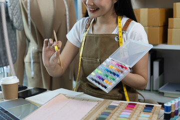 A woman is sewing and smiling. She is holding a spool of thread and a sewing machine
