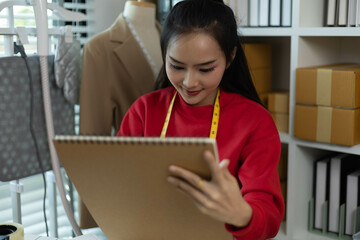 A woman in a red sweater is sitting at a desk with a laptop and a notebook. She is smiling and she...