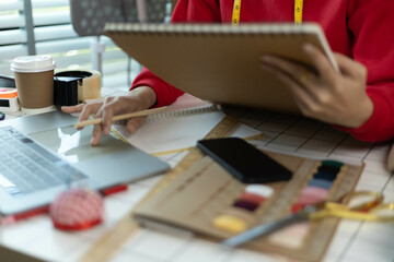 A woman in a red sweater is sitting at a desk with a laptop and a notebook. She is smiling and she...