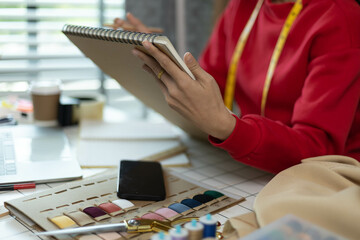 A woman in a red sweater is sitting at a desk with a laptop and a notebook. She is smiling and she...
