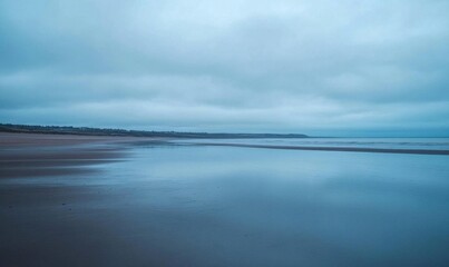 Obraz premium A serene beach scene under a cloudy sky, reflecting calm waters.