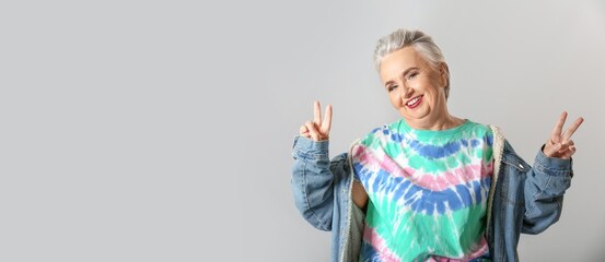Stylish elderly woman showing victory gesture on grey background with space for text