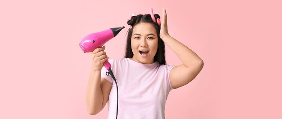 Happy Asian woman with hair dryer on pink background