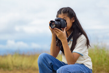 Asian girl uses digital camera to take photos of nature in a field. Concept of exploration, outside the classroom, outdoors, ecology, nature, learning, travel.