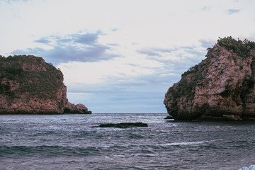 A dreamy coastal view of Taormina, Sicily, featuring dramatic cliffs, calm Mediterranean waters, and a soft sky at dusk, capturing the tranquil beauty of nature and summer paradise.