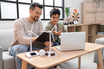 Teenage boy and his father writing in clipboard with wind turbine models at home