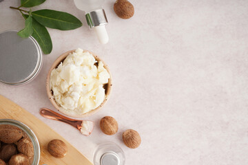 Composition with bowl of shea butter, nuts and cosmetic products on light background
