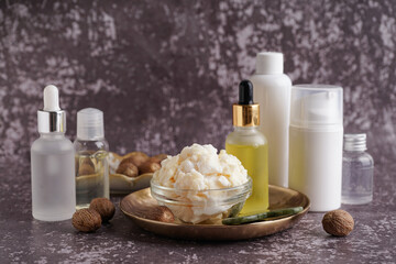 Composition with bowl of shea butter and cosmetic products on grunge background