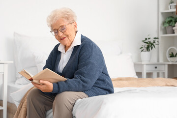 Happy senior woman reading book in bedroom at home