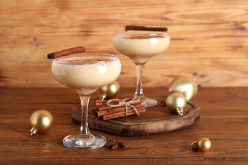 Glasses of tasty eggnog cocktail with cinnamon and Christmas balls on wooden background