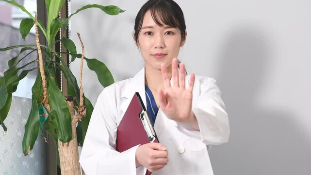 STOPポーズをする白衣姿のアジア人女性