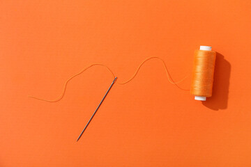 Thread spool with needle on orange background