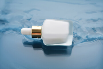 Bottle with white moisturizing serum in water on blue background.