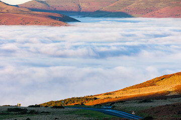 Small, winding rural road leading towards a fog filled valley below (Wales, UK)