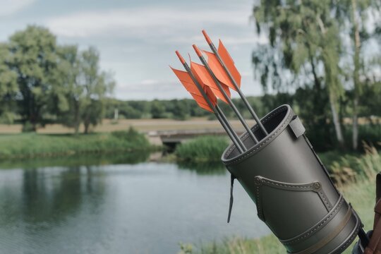 Arrows with orange fletching in a quiver by a lake, serene outdoors.