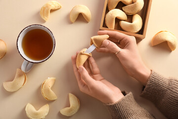 Female hands with broken fortune cookie and cup of tea on beige background