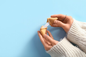 Female hands with broken fortune cookie on blue background