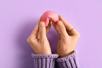 Female hands with pink fortune cookie on lilac background